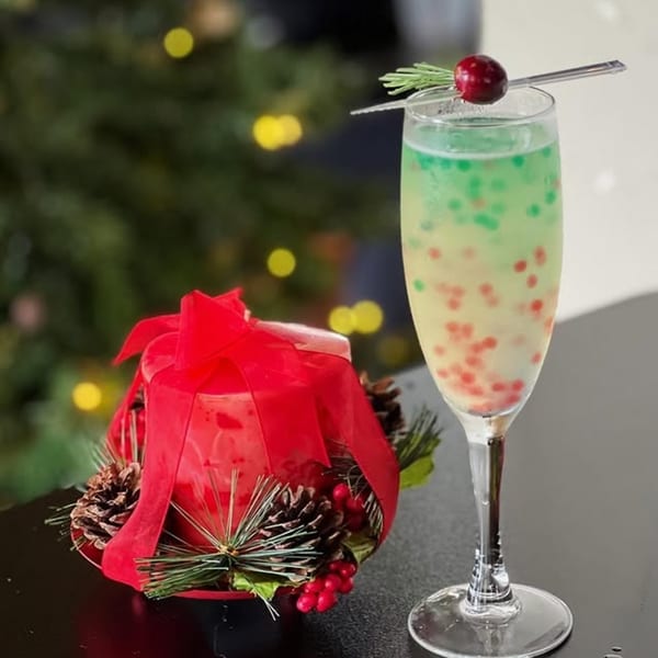 A festive Miyo's Restaurant cocktail with green and red boba, garnished with rosemary and a cranberry.