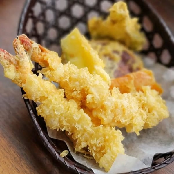 Crispy golden tempura shrimp and vegetables served in a dark woven basket at Miyo's Restaurant.