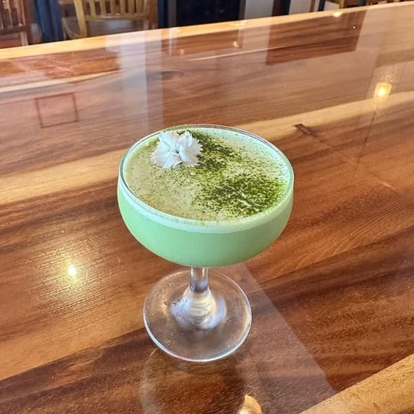 A green matcha cocktail with a white flower garnish sits on a glossy wooden bar at Miyo's Restaurant.