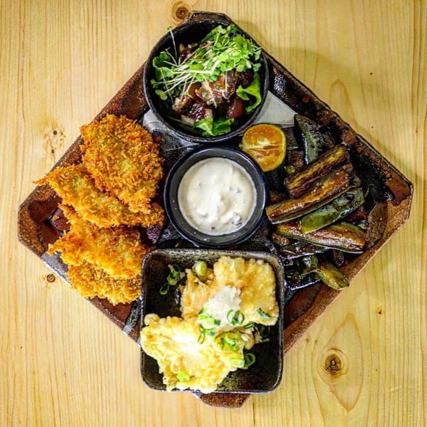 A Japanese appetizer platter with fried cutlets, tempura, grilled vegetables, and a small salad.