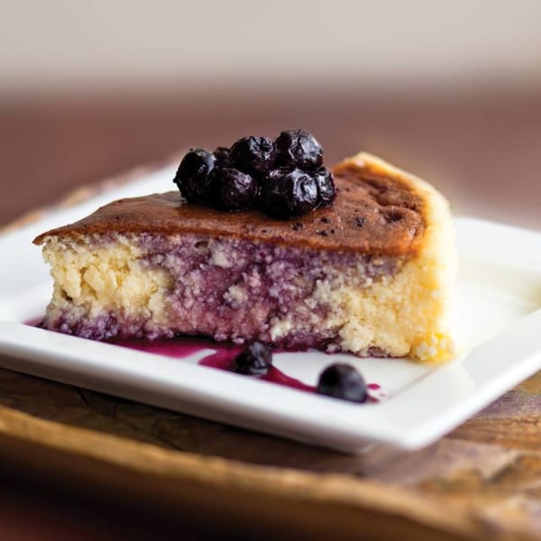 A slice of blueberry cheesecake with a blueberry topping and sauce on a white plate.