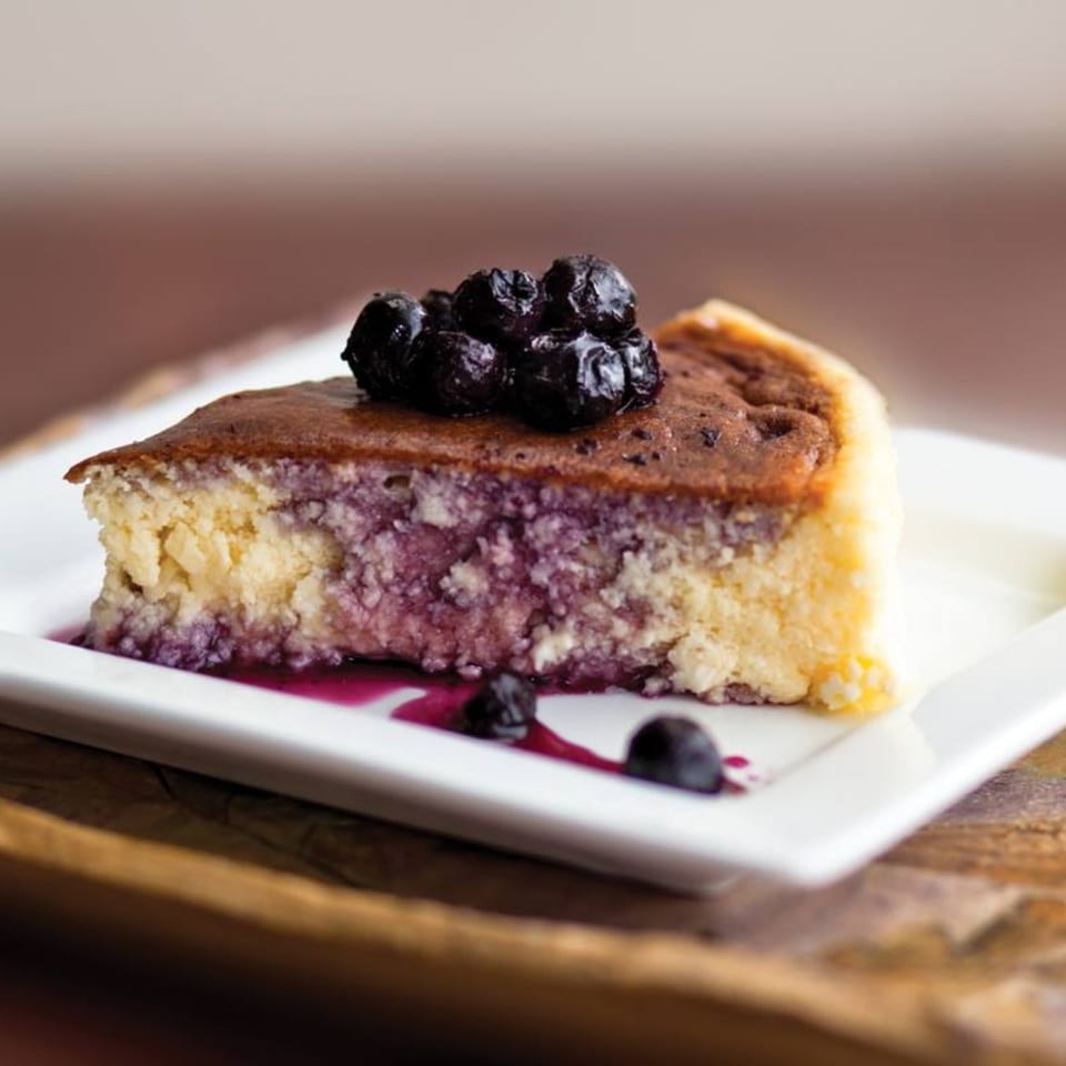 A slice of blueberry cheesecake with a blueberry topping and sauce on a white plate.