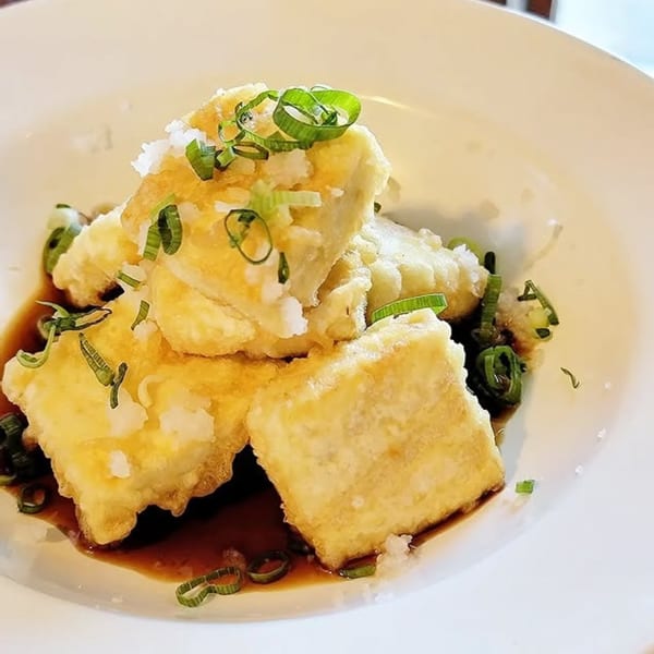 Crispy fried tofu squares with dark sauce, garnished with grated daikon and chopped green onions.