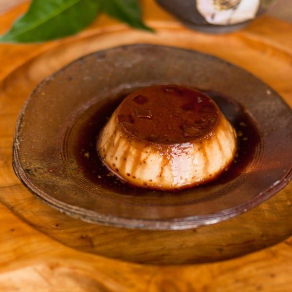 A Japanese flan dessert with dark caramel sauce on a rustic brown plate.