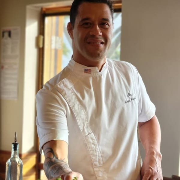 Miyo's Restaurant chef in a white uniform with an American flag patch, smiling.
