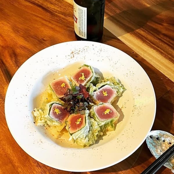 Miyo's Restaurant's seared tuna sashimi with greens and a beer on a wooden table.